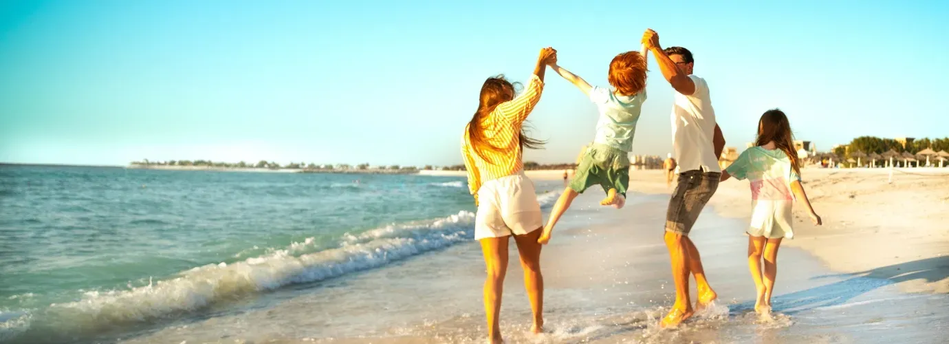 Frau, Mann und zwei Kinder laufen am Strand entlang